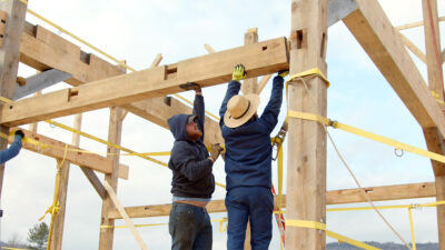 Workers raising a beam on a Legacy Barns historically precise recreation.